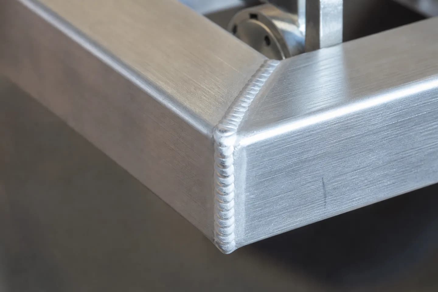 Close-up of a bright, evenly rippled TIG weld bead running around a mitred aluminium square tube corner