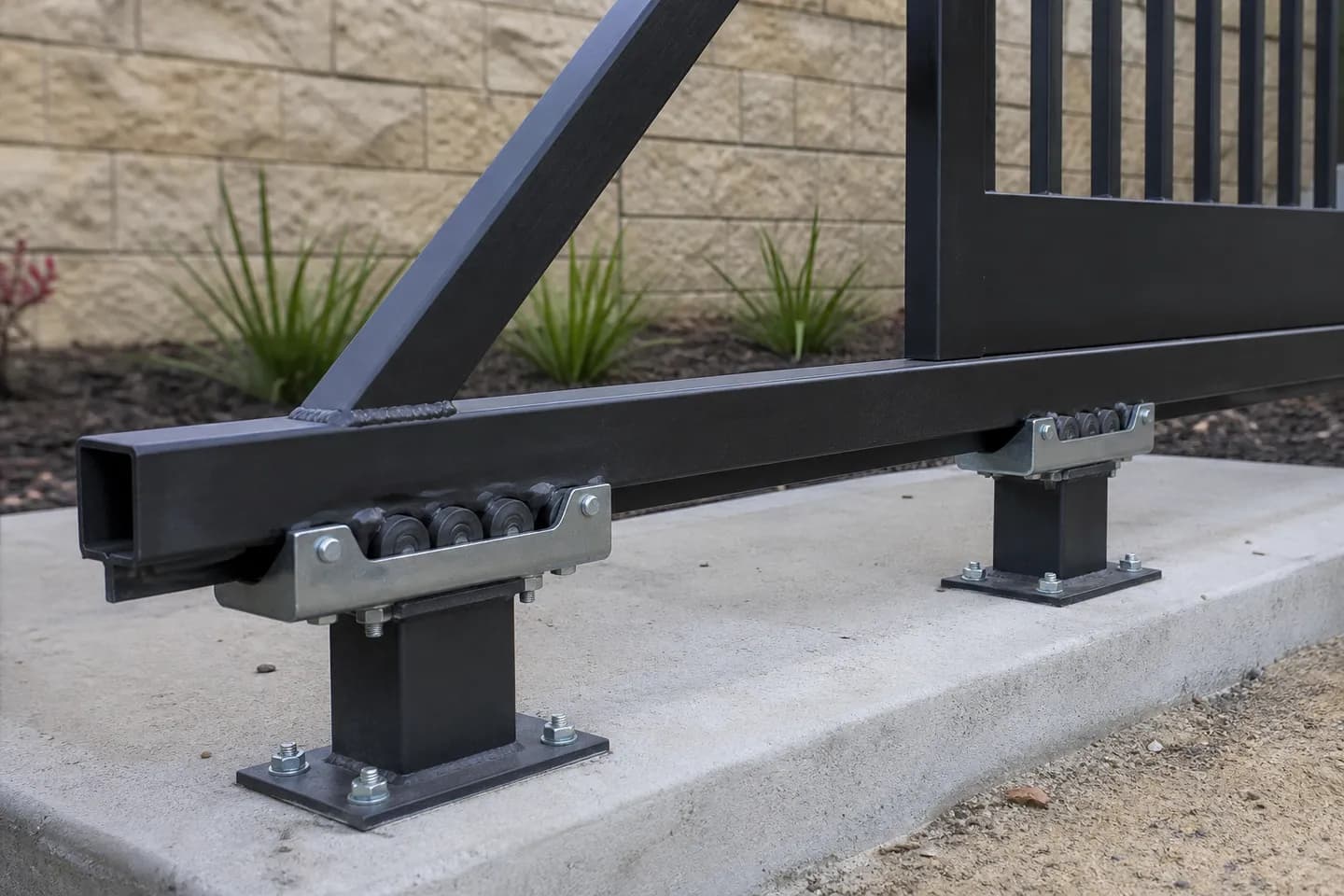 The braced tail of a black aluminium cantilever gate running through two roller carriages on short square posts beside a driveway
