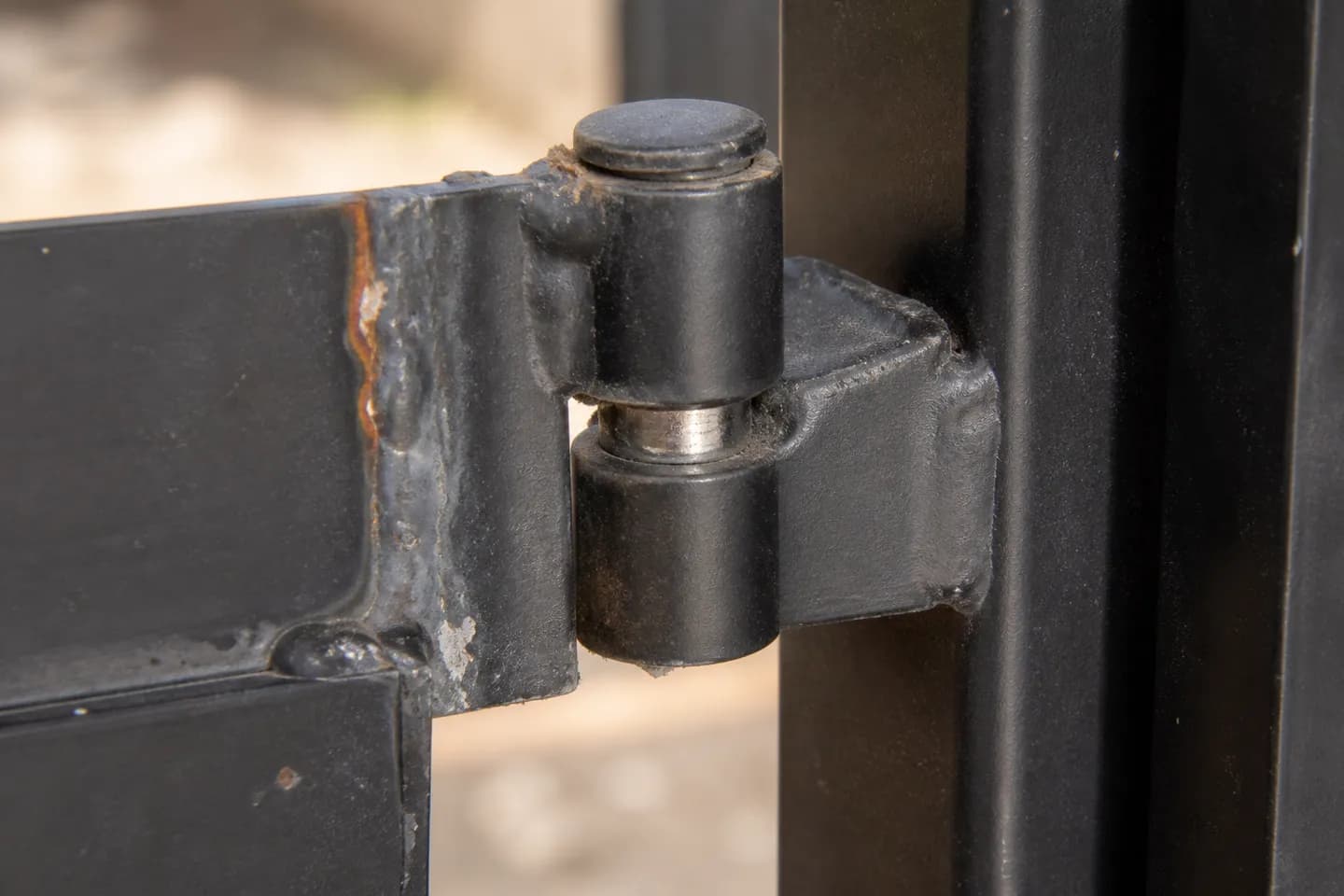 Close-up of a worn weld-on barrel hinge with a gap between its knuckles and bare metal on the pin