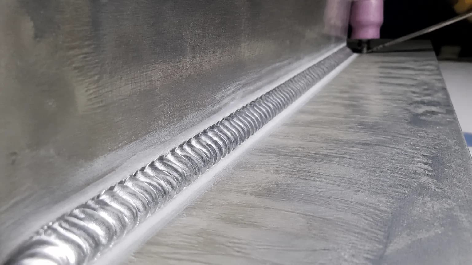 Close-up of a bright, rippled TIG fillet weld joining two pieces of aluminium at a T-joint
