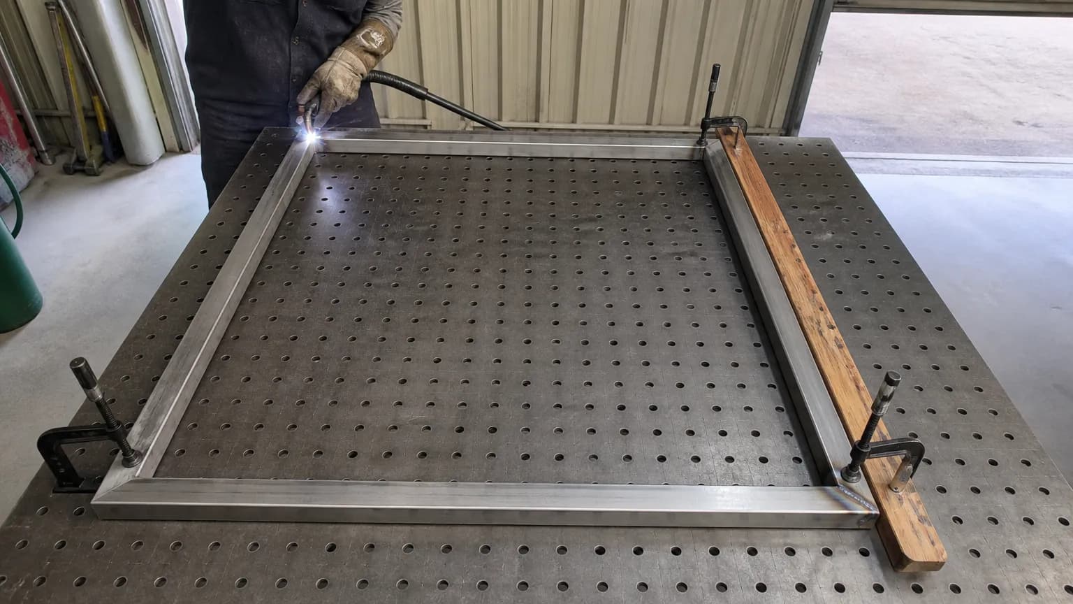 An aluminium gate frame clamped to a fabrication table with F-clamps at every corner while one corner is welded