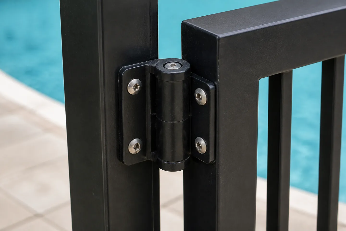 A black polymer self-closing gate hinge screwed to a black square aluminium pool fence post, with the vertical bars of the gate beside it