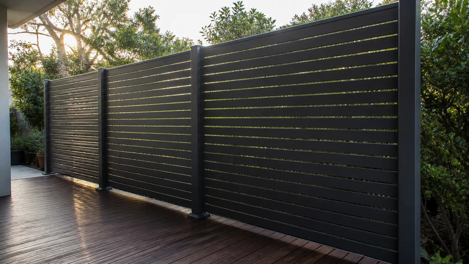 A charcoal horizontal aluminium slat screen with even narrow gaps around a backyard deck, afternoon light through the gaps
