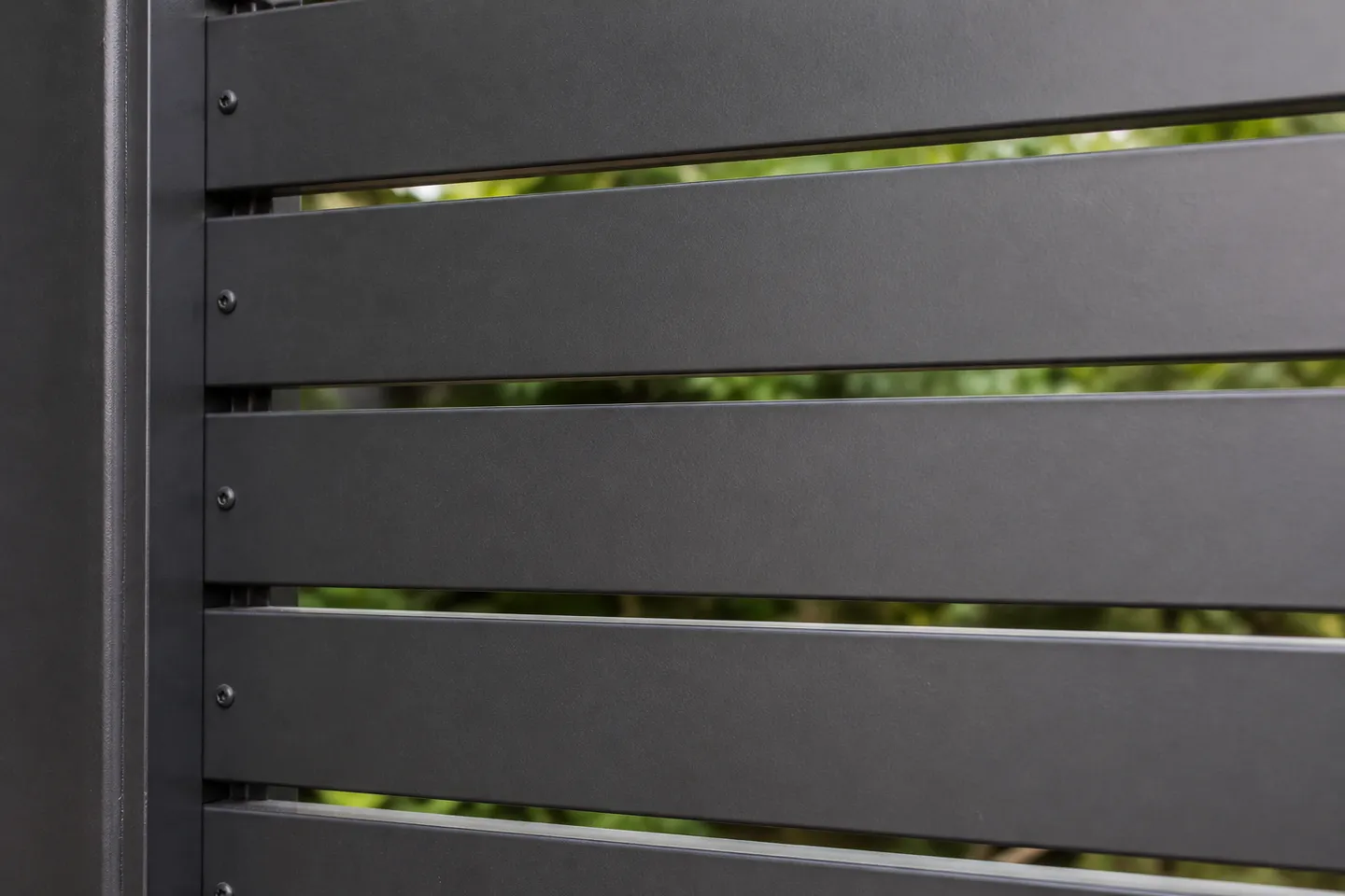 Close-up of a charcoal horizontal aluminium slat screen with narrow even gaps and soft garden light coming through