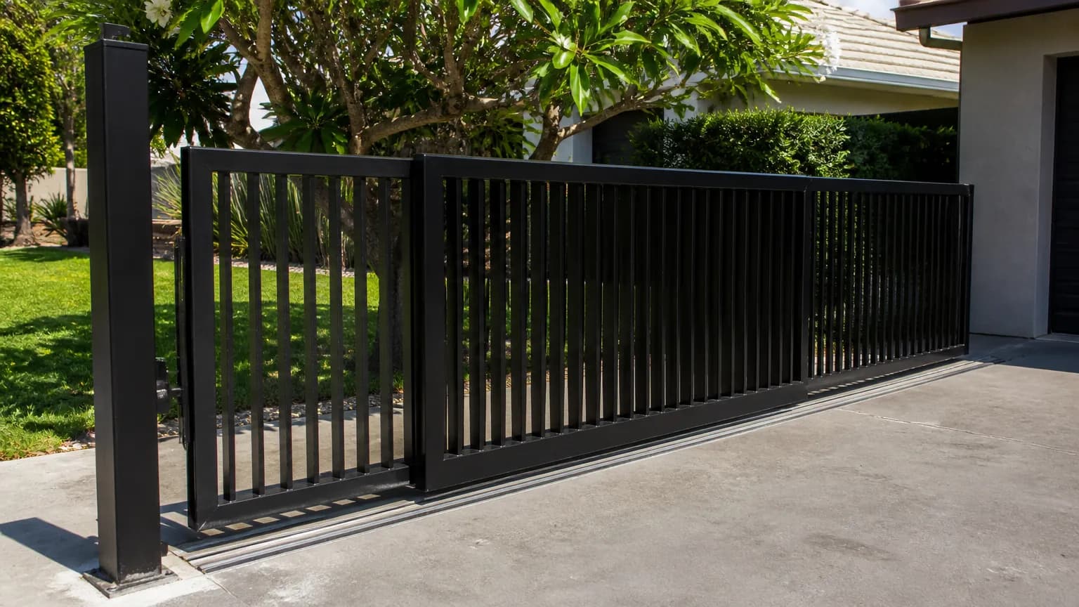 A two-leaf black aluminium battened telescopic sliding gate half open across a wide driveway, one leaf sliding behind the other