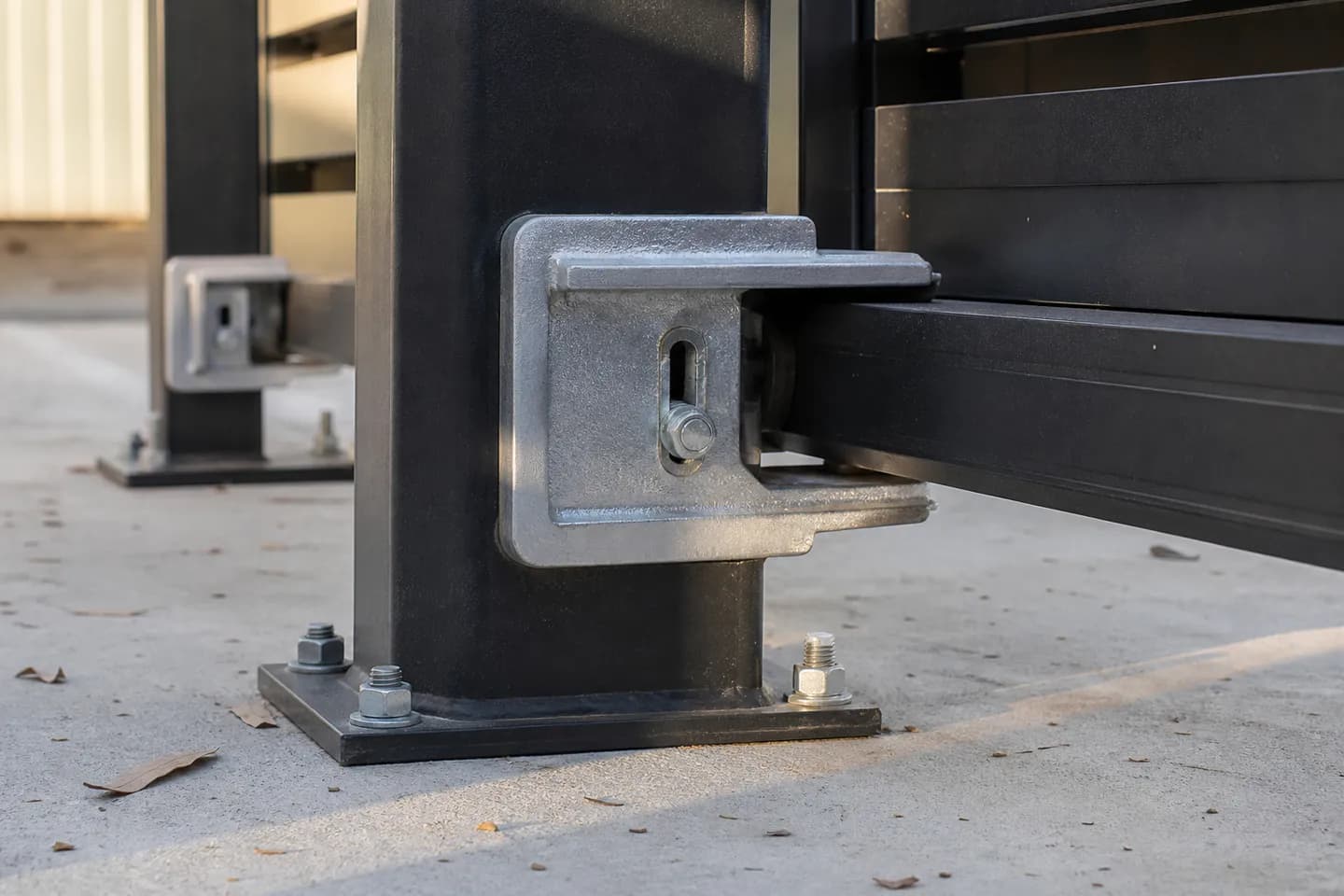 Close-up of a cantilever gate roller carriage on a galvanised post, the gate's bottom rail running through it above a concrete driveway