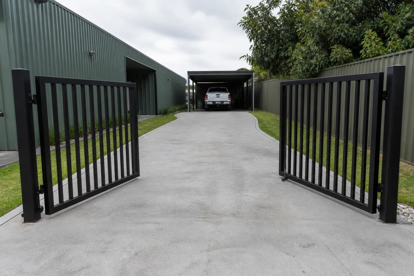 A black aluminium double swing driveway gate with both leaves open inward over a flat concrete driveway